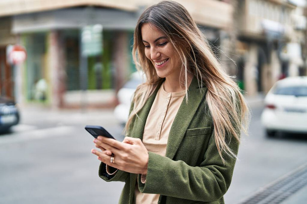 Mujer joven sonriendo confiada usando teléfono inteligente en la calle - Foto, imagen