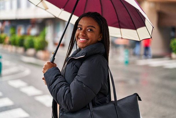 afro-américaine femme souriant confiant en utilisant parapluie à la rue - Photo, image