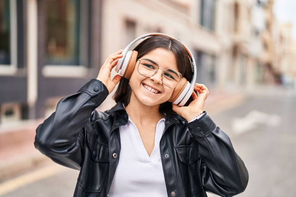 Mladý krásný hispánec žena usměvavý jistý poslech hudby na ulici - Fotografie, Obrázek