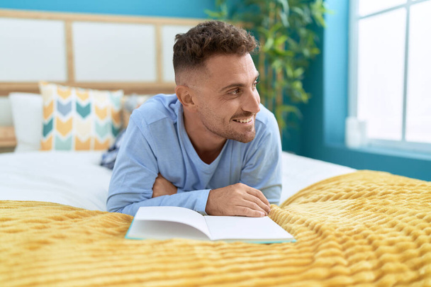 Young hispanic man reading book lying on bed at bedroom - Photo, Image