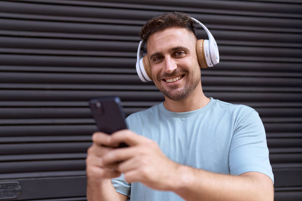 Young hispanic man listening to music over isolated black metal background - Photo, Image