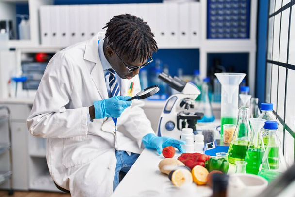 Afrikaanse Amerikaanse man wetenschapper op zoek tomaat met behulp van loupe op laboratorium - Foto, afbeelding