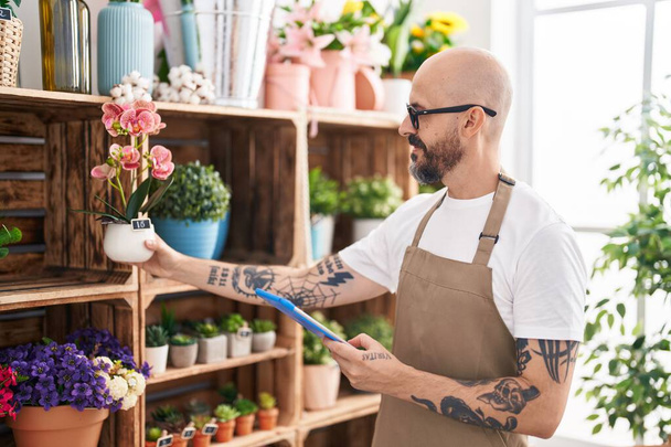 Young bald man florist using touchpad holding plant at florist - Фото, изображение