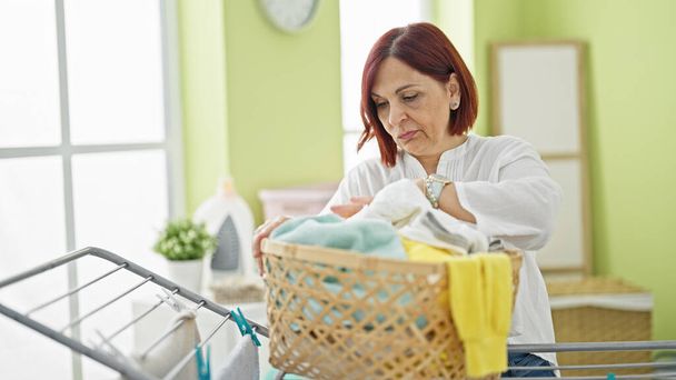 Frau mittleren Alters sucht Kleidung auf Korb in Waschküche - Foto, Bild