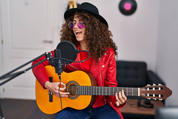 Joven mujer hispana músico cantando canción tocando guitarra clásica en el estudio de música - Foto, imagen