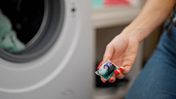 Mujer rubia joven lavando ropa sosteniendo bolsa de detergente en la sala de lavandería - Foto, Imagen