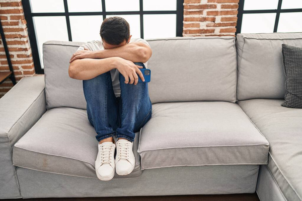Νεαρός Ισπανός στρεσαρισμένος κάθεται στον καναπέ στο σπίτι - Φωτογραφία, εικόνα