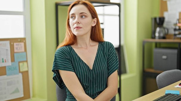 Young redhead woman business worker sitting on table looking to the side at office - Photo, Image
