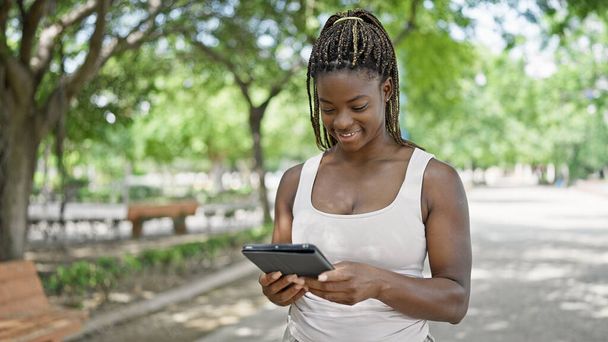Mujer afroamericana sonriendo confiada usando touchpad en el parque - Foto, Imagen