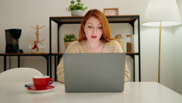 Jeune rousse femme utilisant un ordinateur portable boire du café à la maison - Photo, image