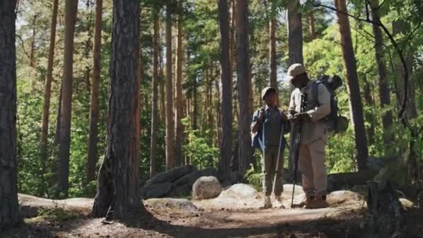 Largo tiro de hombre mayor activo y su nieto senderismo en el bosque de montaña utilizando brújula para encontrar la dirección - Metraje, vídeo