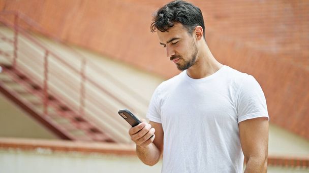 Nuori latino mies käyttää älypuhelinta, jolla on vakava ilme kadulla - Valokuva, kuva