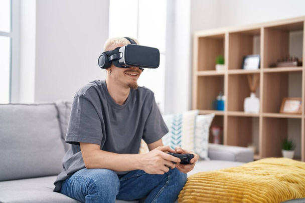 Young caucasian man playing video game using virtual reality glasses at home - Foto, imagen