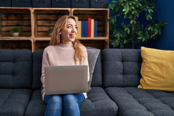Fiatal nő használja laptop ül kanapén otthon - Fotó, kép