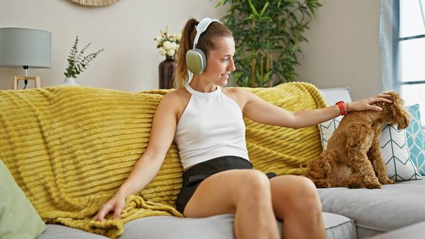 Young caucasian woman with dog sitting on the sofa wearing headphones at home - Foto, Bild