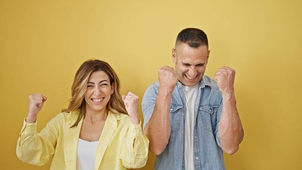 man en vrouw paar glimlachen zelfverzekerd staan samen vieren over geïsoleerde gele achtergrond - Foto, afbeelding