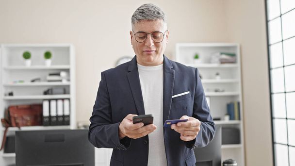 Nuori valkoihoinen mies liiketoiminnan työntekijä ostoksilla älypuhelimen ja luottokortin toimistossa - Valokuva, kuva