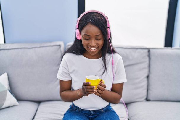 若いアフリカ系アメリカ人女性は自宅でコーヒーを飲む音楽を聞いて - 写真・画像