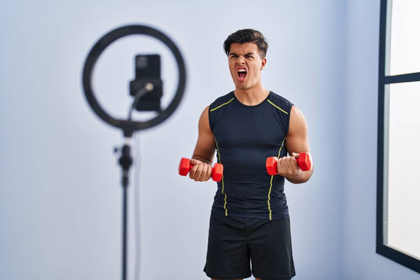 Homem hispânico gravando tutorial de treinamento no ginásio irritado e louco gritando frustrado e furioso, gritando com raiva. raiva e conceito agressivo.  - Foto, Imagem