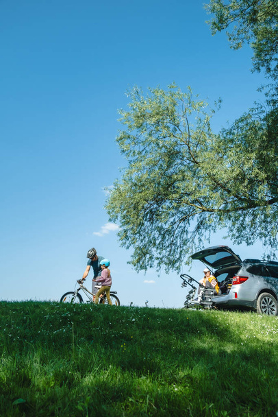 счастливая семья на открытом воздухе отец учит дочь ваш велосипед мать сидит в багажнике автомобиля копировать пространство - Фото, изображение
