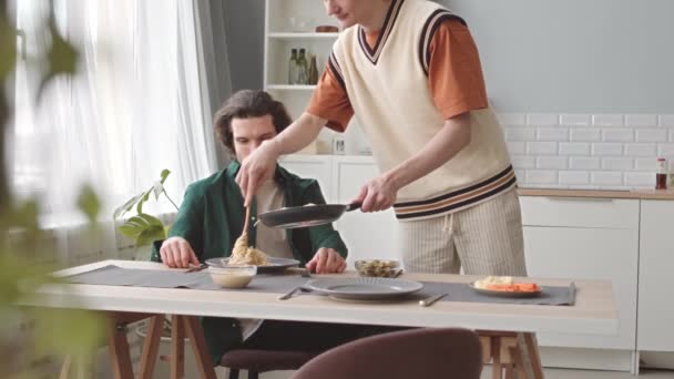 Valkoihoinen homo mies tarjoilee kotitekoista pastaa romanttiselle kotipäivälliselle rakkaan kumppaninsa kanssa. - Materiaali, video