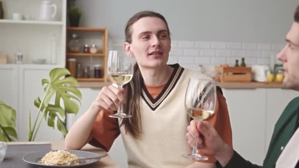 Kiintoisa nuori valkoihoinen homopari paahtaa viinilasien kanssa romanttisella illallisella kotona. - Materiaali, video