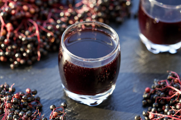 Чорний сироп бузини в склянці зі свіжими ягодами на темному фоні - Фото, зображення