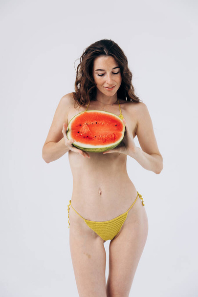 Schlankes, athletisches Mädchen im sommerlichen Badeanzug hält Wassermelone in der Hand. Ruhe, Urlaub am Meer. Frauengesundheit - Foto, Bild