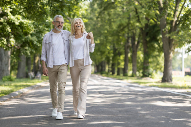 Szerető érett férfi és nő ölelkezve sétálva együtt a parkban, boldog nyugdíjas pár pihentető szabadban, ölelés és mosolygás, élvezi a randit odakinn, teljes hosszúságú felvétel másolási hellyel - Fotó, kép