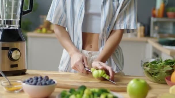 Tilt up shot of young woman putting pieces of fresh kiwi into blender while making fruit smoothie in home - Metraje, vídeo