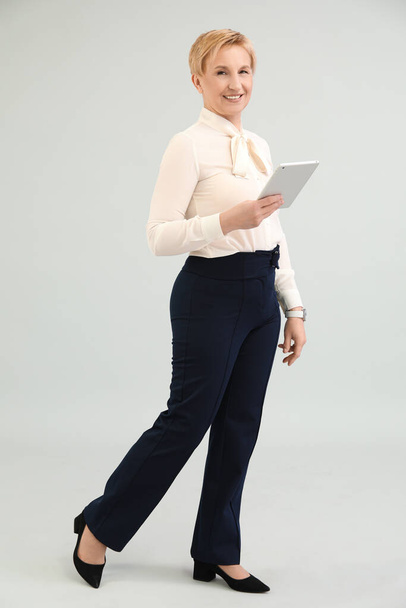 Donna d'affari matura con tablet su sfondo grigio - Foto, immagini