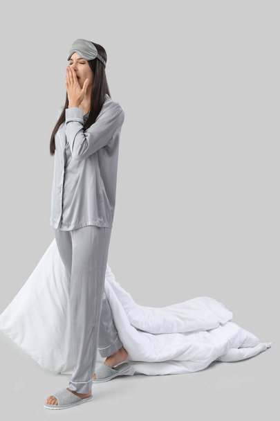 Mooie jonge vrouw met zachte deken en kussen geeuwen op grijze achtergrond - Foto, afbeelding
