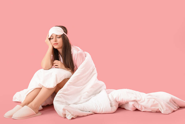 Sleepy young woman with soft blanket sitting on pink background - Photo, Image