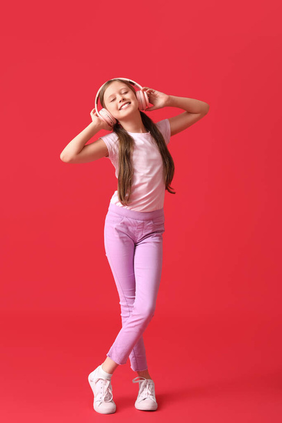 Klein meisje in koptelefoon op rode achtergrond - Foto, afbeelding