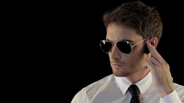 Security man looking to the sides isolated against black background. Brunette man making movements like bodyguard. Cool man in aviator sunglasses taking a look around - Footage, Video