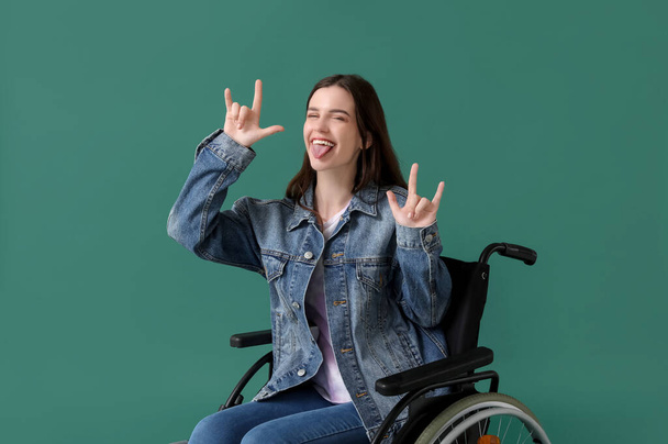 Junge Frau im Rollstuhl zeigt "Teufelshörner" auf grünem Hintergrund - Foto, Bild
