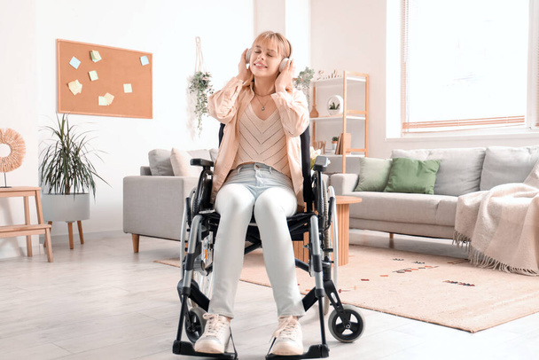 Jonge vrouw met hoofdtelefoon in rolstoel thuis - Foto, afbeelding