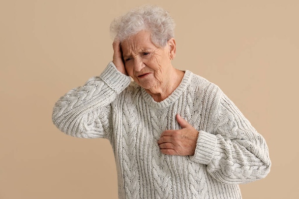 Літня жінка має серцевий напад на бежевий фон - Фото, зображення