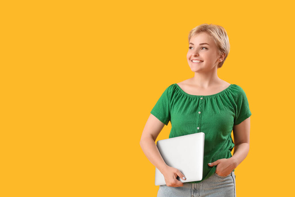 Happy young female programmer with laptop on yellow background - Photo, Image