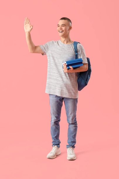 Boldog férfi diák hátizsák és könyvek integető kéz rózsaszín háttér - Fotó, kép