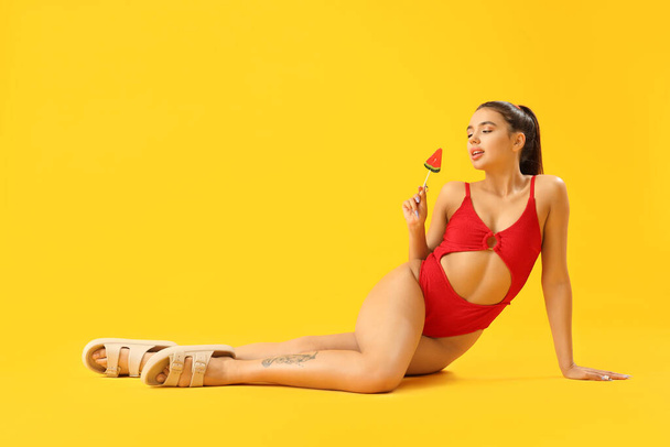 Krásná sexy mladá žena v plavkách a s vodní meloun lízátko na žlutém pozadí - Fotografie, Obrázek
