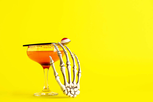 Verre de savoureux cocktail Margarita pour Halloween avec la main squelette sur fond jaune - Photo, image