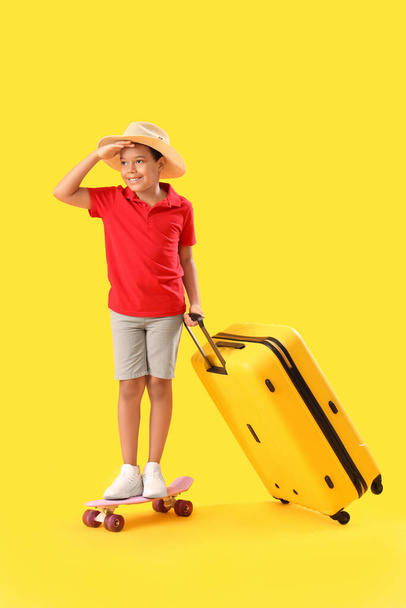 Μικρό Αφροαμερικανό αγόρι με βαλίτσα και σκέιτμπορντ σε κίτρινο φόντο - Φωτογραφία, εικόνα