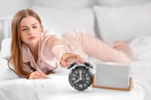 Nuori nainen sängyssä tavoittelemassa herätyskelloa makuuhuoneessa - Valokuva, kuva