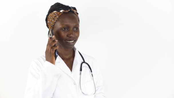 白い背景で孤立した彼女の携帯電話で話す若い女性の医師  - 映像、動画