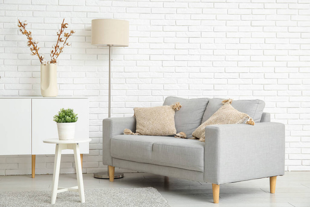 Interiér světlého obývacího pokoje s šedou pohovkou, standardní lampou a bílým příborníkem - Fotografie, Obrázek
