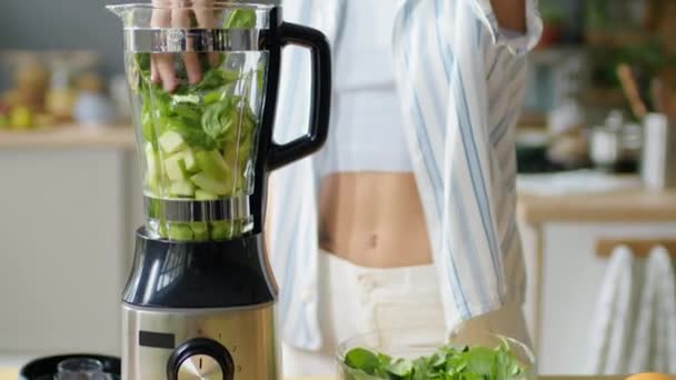 Nakloň oříznutý záběr ženy, jak dává čerstvé salátové listy do mixéru a zavírá víko před přípravou zeleného smoothie v kuchyni doma - Záběry, video