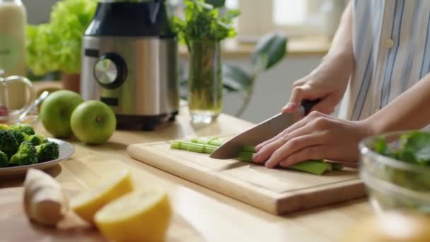 Primer plano plano de manos femeninas cortando tallos de apio fresco en tablero de madera en la mesa de la cocina mientras prepara una cena saludable en casa - Imágenes, Vídeo