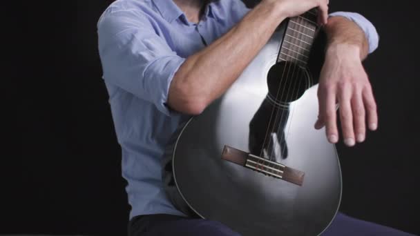 músico masculino con una guitarra en las manos gira en un círculo sobre un fondo oscuro, de planta media - Metraje, vídeo