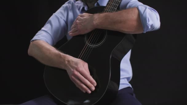 музичний виконавець, чоловік з гітарою в руках б'є ритм на темному фоні - Кадри, відео